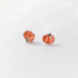 May include: A pair of silver pumpkin earrings. Each earring features a small, orange pumpkin with green stem detailing. The pumpkins have silver outlines and are set against a white background.