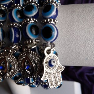 May include: A multi-strand bracelet with blue and white evil eye beads and a silver charm with a hamsa hand and a blue evil eye in the center.