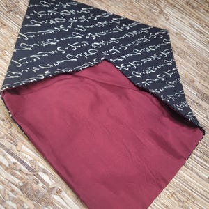 May include: A reversible bandana. The outer layer is dark navy blue, printed with white cursive script. The inner layer is a solid burgundy colour. The bandana is folded in a diamond shape, displaying both sides.
