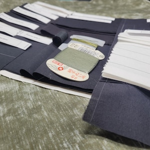 May include: A close-up of a fabric swatch book with a variety of black and white fabric swatches. A spool of green thread is visible in the center of the image. The text on the spool reads "40番  濃緑"