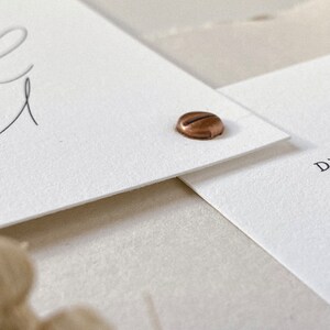May include: Two white cards with a copper colored metal fastener. The top card has a handwritten word on it.