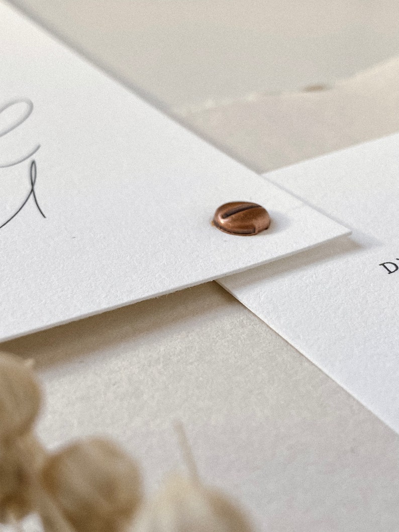 May include: Two white cards with a copper colored metal fastener. The top card has a handwritten word on it.