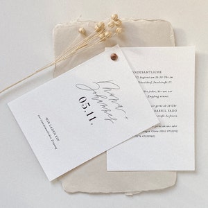 May include: A white wedding invitation with black calligraphy text. The text reads "Phone Johannes 05.11. WIR LADEN EIN zur standesamtlichen Trauung" and "ANDESAMTLICHE G beginnt um 16:30 Uhr im D&uuml;sseldorf, Inselstra&szlig;e 17. ber jeden, der uns vor Empfang nimmt. wir gerne ab 18 Ubr BARRIL FADO stra&szlig;e 2a feiern. gerne an uns oder tugen Clara (0163 9732291) (0176 43220968)."