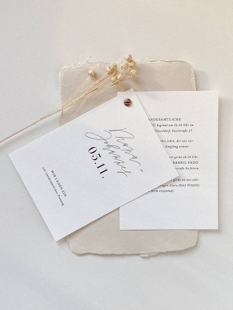 May include: A white wedding invitation with black calligraphy text. The text reads "Phone Johannes 05.11. WIR LADEN EIN zur standesamtlichen Trauung" and "ANDESAMTLICHE G beginnt um 16:30 Uhr im D&uuml;sseldorf, Inselstra&szlig;e 17. ber jeden, der uns vor Empfang nimmt. wir gerne ab 18 Ubr BARRIL FADO stra&szlig;e 2a feiern. gerne an uns oder tugen Clara (0163 9732291) (0176 43220968)."