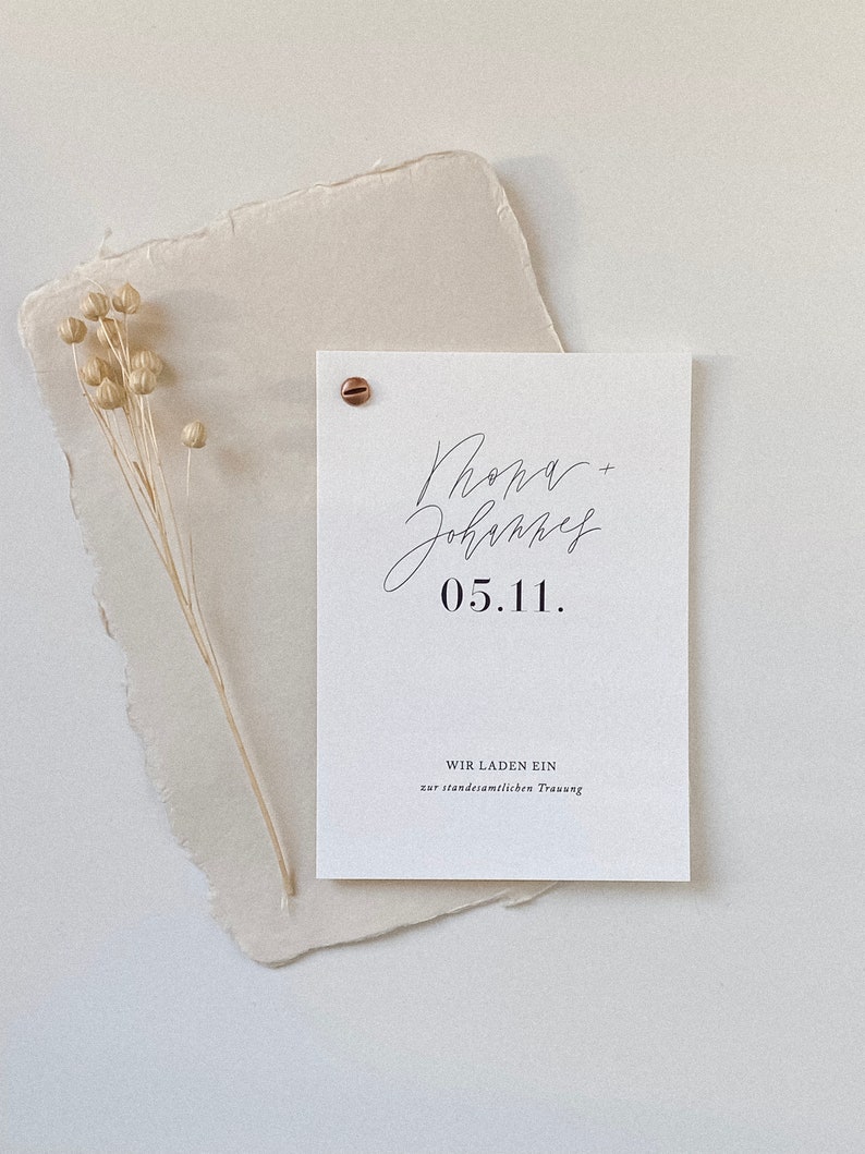 May include: A white card with black text announcing a wedding. The card reads "Phona + Johannes 05.11. WIR LADEN EIN zur standesamtlichen Trauung."