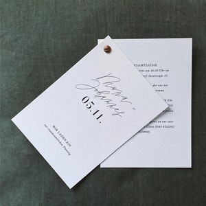 May include: A white wedding invitation with black text. The invitation reads "We are getting married on 05.11.  We invite you to our wedding ceremony at 4:30 PM at Inselstra&szlig;e 17.  We will celebrate afterwards at 8:00 PM.  Please RSVP to Clara at (0163) 9732291 or (0322) 20968."