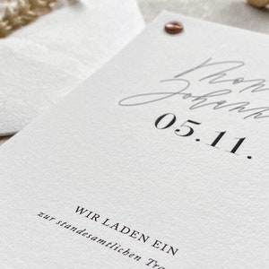 May include: A white card with black text that reads "Wir laden ein zur standesamtlichen Trauung" and "05.11."