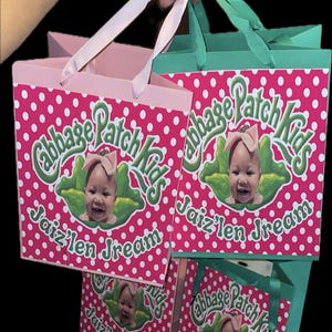 May include: Pink and green gift bags with white polka dots. The bags feature the text "Cabbage Patch Kids" and "Jaiz'len Dream" with a baby's face. The bags have pink and green handles.