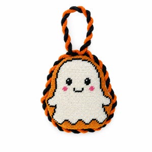 May include: A cross-stitched ornament featuring a white ghost with black eyes and pink cheeks, centred on an orange background. The ornament is framed by a twisted orange and black rope border and includes a matching twisted rope loop for hanging.