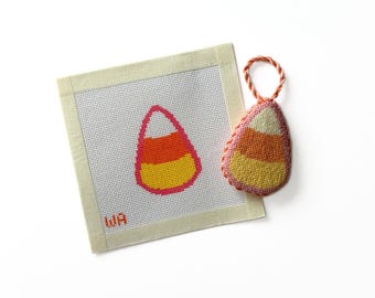 May include: A square needlepoint canvas featuring a stitched candy corn design with a pink outline and the letters WA in the corner, accompanied by a three-dimensional, stuffed candy corn ornament with a matching orange twisted cord loop.
