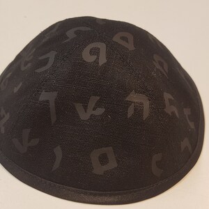 Pu&ograve; includere: Una kippah nera con un motivo di alfabeto ebraico.