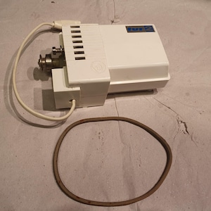 May include: A white Tur 2 sewing machine motor with a metallic drive pulley, a white power cord, and a separate brown rubber drive belt. The motor housing features a rectangular blue label with the text Tur 2 and a circular embossed logo.