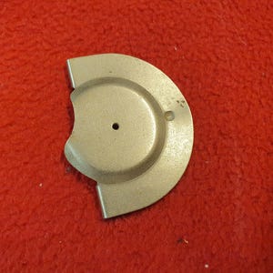 May include: A silver-colored, semi-circular metal object with a circular indentation and a small hole. The object is set against a red, textured background.