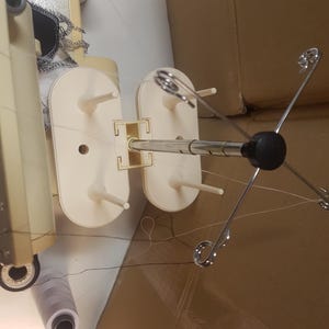 May include: A white sewing machine with a white thread stand and a silver thread holder. The thread holder has four arms that extend out from the center.