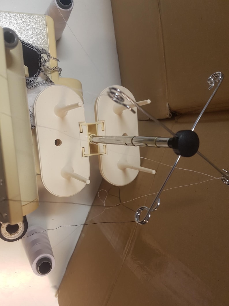 May include: A white sewing machine with a white thread stand and a silver thread holder. The thread holder has four arms that extend out from the center.
