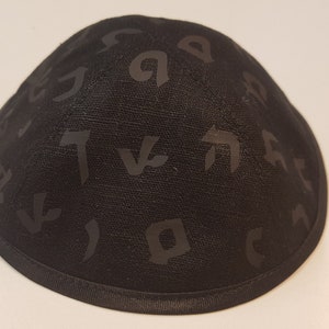 Pu&ograve; includere: Una kippah nera con un motivo di lettere ebraiche.