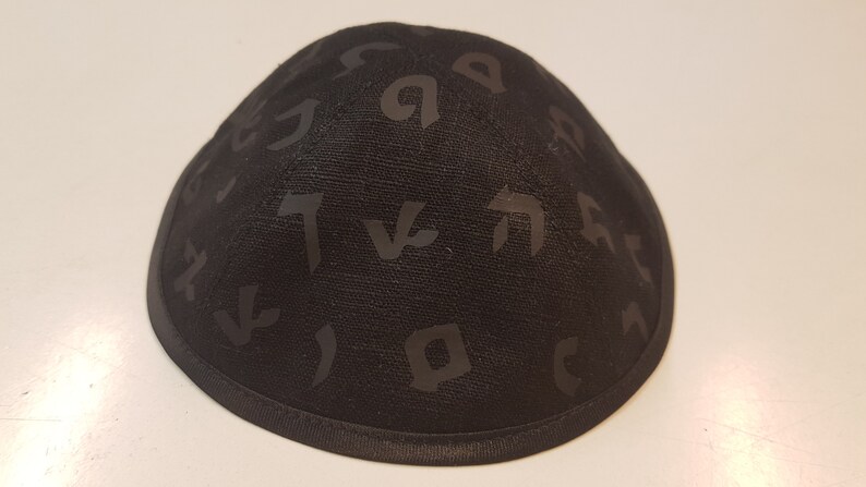 Pu&ograve; includere: Una kippah nera con un motivo di lettere ebraiche.