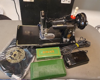 Puede incluir: Una máquina de coser Singer negra vintage con detalles dorados, un pedal y una funda de transporte. La máquina tiene una base negra y una cubierta negra. Accesorios: una caja verde y un estuche negro.