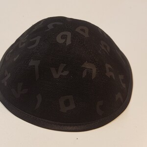 Pu&ograve; includere: Una kippah nera con un motivo di alfabeto ebraico.
