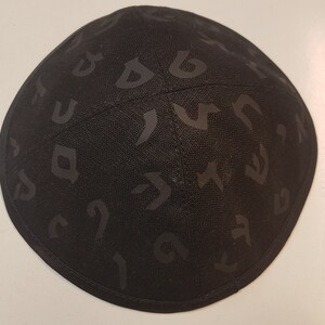 Pu&ograve; includere: Una kippah nera con un motivo di alfabeto ebraico.