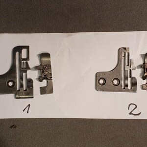 Könnte beinhalten: Zwei Metallteile einer Nähmaschine, beschriftet mit 1 und 2, werden auf weißem Papier gezeigt. Die silberfarbenen Teile weisen komplizierte mechanische Details auf, darunter Schrauben und geschlitzte Abschnitte. Der Hintergrund ist eine dunkle, strukturierte Oberfläche.