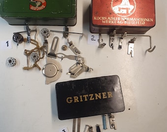 May include: An assortment of vintage sewing machine parts and accessories, including metal boxes with the Singer, Kochs Adler, and Gritzner logos. Various attachments, bobbins, and presser feet are scattered around the boxes, suggesting a collection of sewing tools.