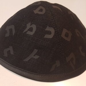 Pu&ograve; includere: Una kippah nera con un motivo di lettere ebraiche.
