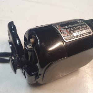 Puede incluir: Un motor de máquina de coser negro con una etiqueta plateada. La etiqueta incluye texto como "SEWING MOTOR", "115-125 VOLTS" y "SIMANCO. GREAT BRITAIN."