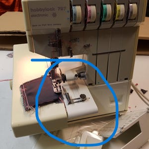 Può includere: Macchina da cucire taglia e cuci elettronica HobbyLock 797 beige e bianca. La macchina ha più quadranti con accenti colorati e sta cucendo un piccolo pezzo di tessuto. Prodotta in Germania Ovest.