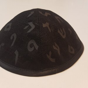 Pu&ograve; includere: Una kippah nera con un motivo di lettere ebraiche. La kippah &egrave; realizzata in un tessuto morbido e testurizzato e ha un bordo in raso nero.