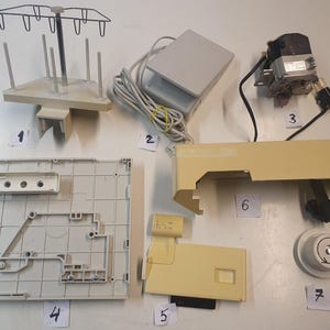 May include: An assortment of sewing machine parts, including a thread spool holder, foot pedal, motor, and various beige plastic components. The parts are arranged on a white surface.
