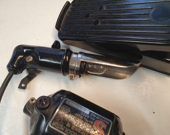 May include: Black Singer sewing machine parts, including a foot pedal, motor, and light assembly. The light assembly has a clear bulb. The motor has a label with text. The foot pedal is black and has a ribbed design.