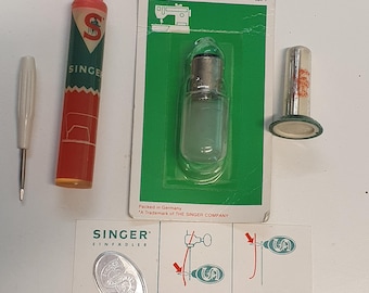 May include: A collection of sewing accessories including a small white screwdriver, a red and green Singer oil tube, a 15W 220V Singer light bulb in its original packaging, a metal thimble, and a Singer needle threader with instructional diagrams.