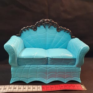Può includere: Un divano in miniatura azzurro con un design a ragnatela sullo schienale e sulla seduta. Il divano ha un rivestimento decorativo nero con un ragno in cima. Un metro a nastro è accanto al divano.