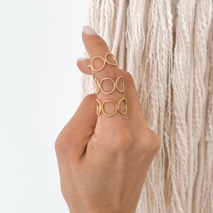 May include: Gold ring with a design of multiple interlocking circles. The ring is worn on the index finger.