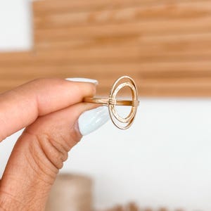 May include: Gold ring with a double circle design. The ring is textured and has a minimalist style.