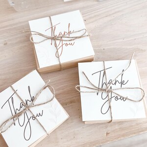 May include: Three small gift boxes with the words "Thank You" written on them. The boxes are wrapped in brown paper and tied with twine.