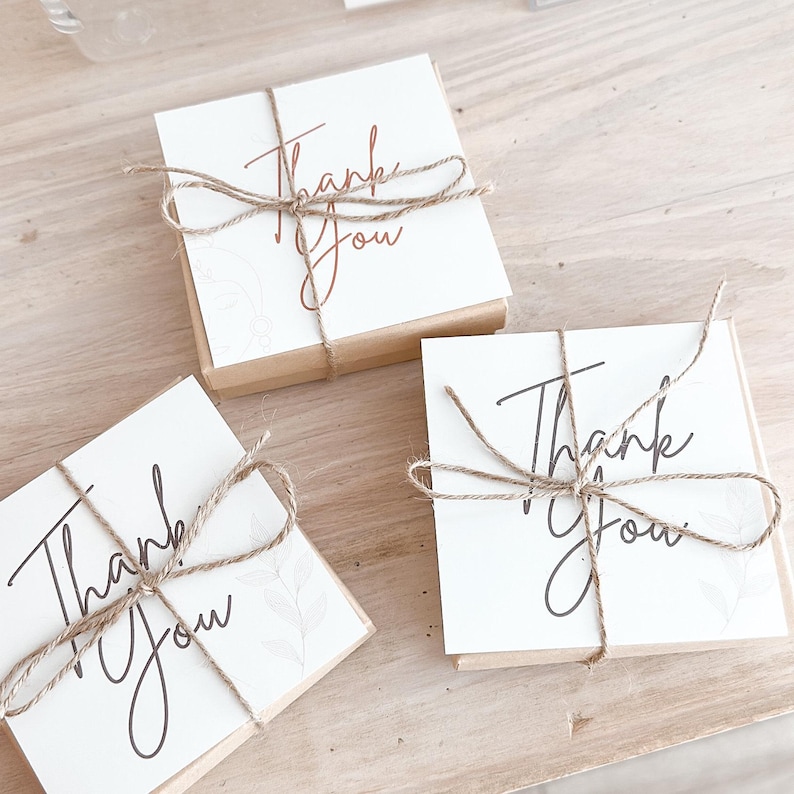 May include: Three small gift boxes with the words "Thank You" written on them. The boxes are wrapped in brown paper and tied with twine.