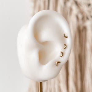 Close-up of 10K gold moon stud earring on silicone ear model, showing size and fit for ear stacking or piercings.