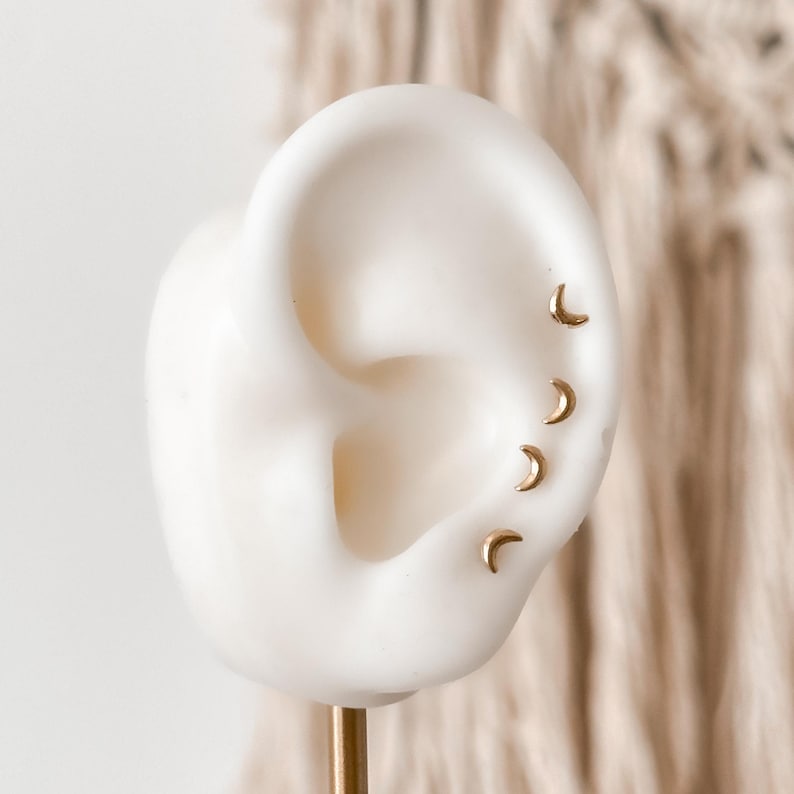Close-up of 10K gold moon stud earring on silicone ear model, showing size and fit for ear stacking or piercings.