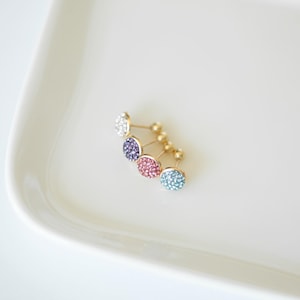 May include: Four pairs of gold stud earrings with round, sparkly stones. The stones are white, purple, pink, and blue.