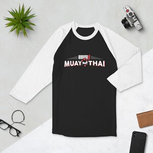 May include: Black and white baseball tee with red and white logo. The logo says "BRAVO 9 MUAY THAI" with a stylized eye graphic.