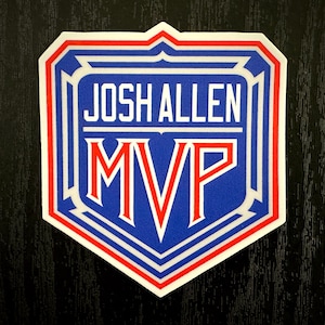 Könnte beinhalten: Blau-rot-weißer Aufkleber mit dem Text "JOSH ALLEN MVP" in weißen Buchstaben. Das Schild-Design hat einen roten Rand und weiße Akzente, ideal für Sportfans.