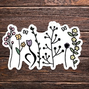 May include: A sticker with a whimsical design of various flowers and plants in shades of pink, yellow, purple, and green. The sticker is on a brown wooden background.