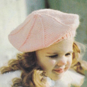May include: A light pink knitted beret hat. The hat is made of a soft, textured yarn and has a classic beret shape. The hat is worn by a person with blonde hair.