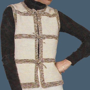 Può includere: Un gilet di maglia color crema con bordi marroni e chiusura a cravatta. Il gilet ha un motivo quadrato ed è senza maniche.