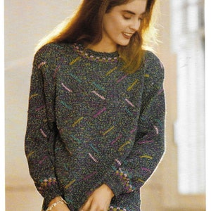 Puede incluir: Una mujer lleva un suéter azul oscuro con un patrón geométrico multicolor. El suéter tiene un cuello redondo y mangas largas.