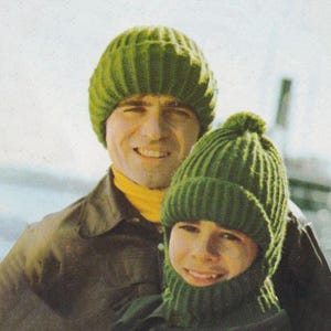 May include: A vintage image of two people wearing matching green knit hats. The hats have a ribbed design. One person is also wearing a green knit scarf. The background is a light, neutral color.