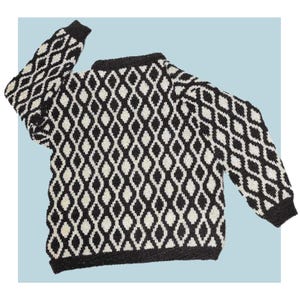 Pode incluir: Um suéter com padrão de losangos em preto e branco. O suéter tem mangas compridas e gola redonda. Os punhos e a gola são pretos. É feito de material de malha.