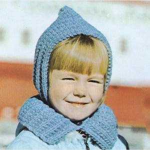 Puede incluir: Un conjunto de capucha y bufanda de ganchillo azul claro. La capucha tiene una parte superior puntiaguda y enmarca la cara. La bufanda es de color azul claro a juego. El conjunto está hecho de hilo texturizado.